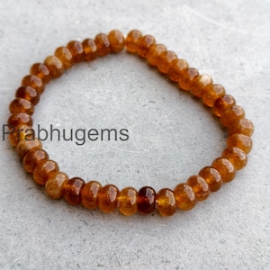 Könnte beinhalten: Ein Armband aus kleinen, runden, bernsteinfarbenen Perlen. Die Perlen sind zu einer kreisförmigen Form aufgereiht. Der Text "Prabhugems" ist auf der linken Seite des Bildes zu sehen. Das Armband liegt auf einer grauen Oberfläche.