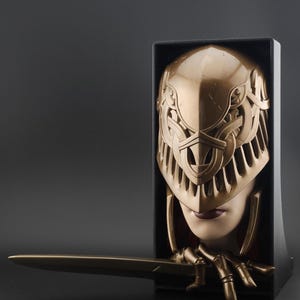 Peut inclure: Sculpture en bronze d'un visage casqué et d'une épée. Le casque, orné de motifs celtiques, ne laisse apparaître que les lèvres. L'épée repose sur un socle noir, accentuant l'aspect dramatique de l'œuvre.