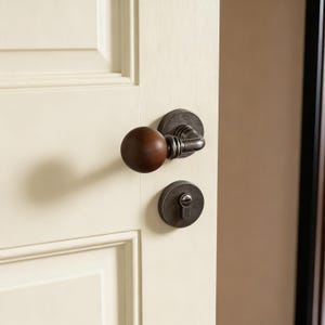Peut inclure: Gros plan sur une porte avec un bouton de porte en bois brun foncé et une serrure en métal foncé. La porte est peinte en crème. Le bouton de porte est rond et la serrure est circulaire.