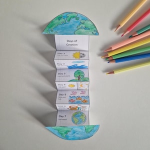 Puede incluir: Una manualidad de papel hecha a mano que representa los días de la creación, con ilustraciones del sol, la luna, el mar, la tierra, las plantas, los pájaros, los peces y la Tierra. El texto "Days of Creation" es visible. Lápices de colores en el fondo.