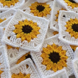 May include: A collection of square crochet motifs featuring a sunflower design. Each motif has a dark brown center, bright yellow petals, and a white square border. The pieces are layered together, showing the intricate yarn texture and pattern.