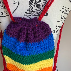 May include: A small rainbow crocheted drawstring bag with red straps. The bag is made with a variety of colors, including purple, blue, green, yellow, orange, and red.