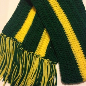 May include: A handmade crochet scarf in green and yellow. The scarf has alternating stripes of dark green and bright yellow. The ends of the scarf have long yellow and green fringe. This cosy scarf is perfect for cold weather.