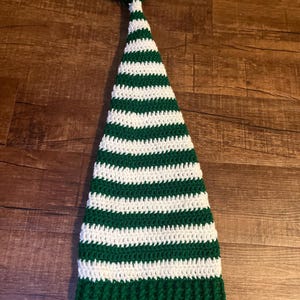 May include: Green and white striped crochet elf hat with a white pom pom on top. The hat has a tag that says "Designed by Tiffany J".