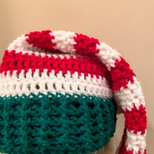 May include: A crocheted Christmas elf hat with a green body and a red and white striped top.