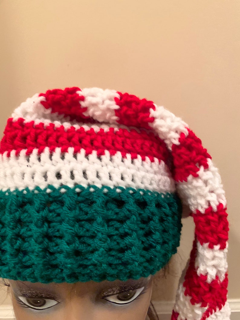 May include: A crocheted Christmas elf hat with a green body and a red and white striped top.