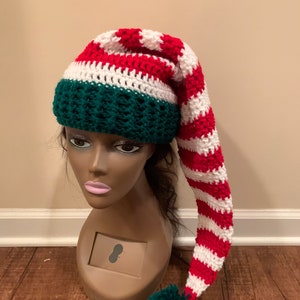 May include: A red and white striped crochet elf hat with a green pom-pom and a green crocheted band.