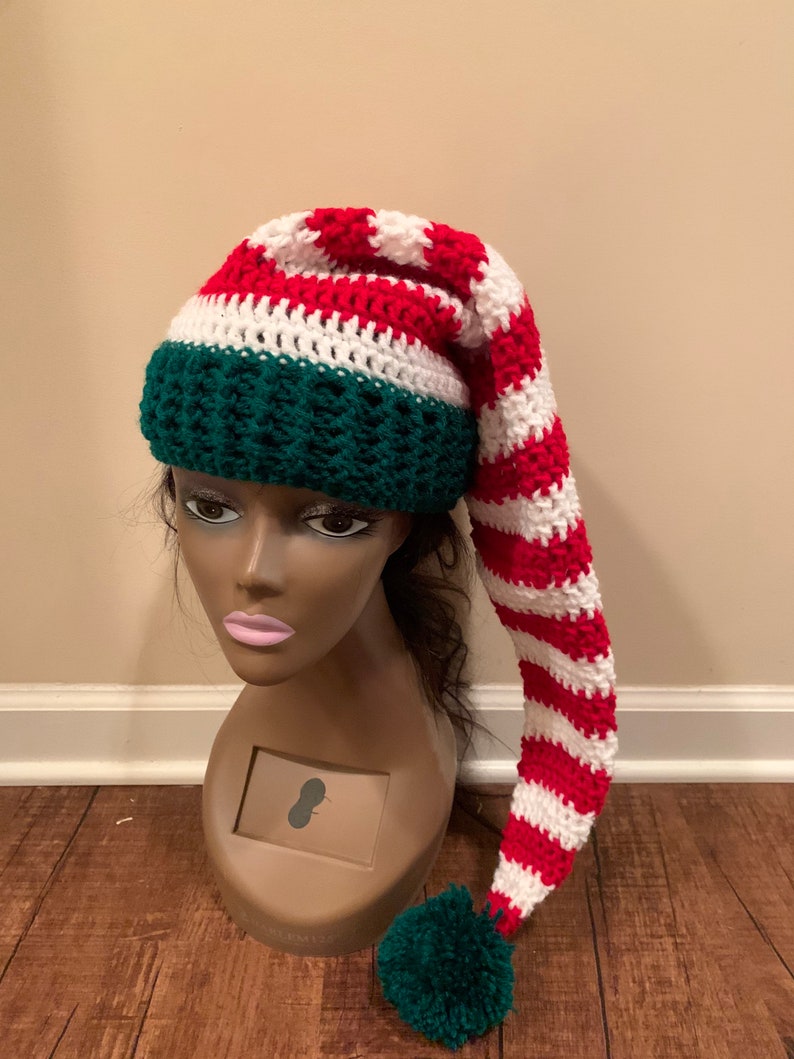 May include: A red and white striped crochet elf hat with a green pom-pom and a green crocheted band.