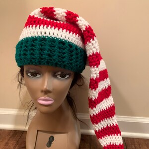 May include: A red and white striped crochet elf hat with a green pom-pom. The hat has a green crocheted band with a white stripe.
