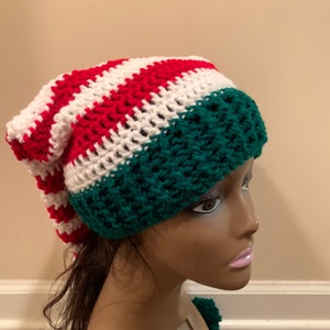 May include: A green, white and red striped crocheted hat with a long tail. The hat is on a mannequin head.