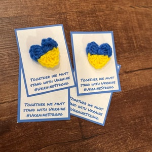 May include: Four cards with crocheted blue and yellow hearts, each with the text "Together we must stand with Ukraine #Ukrainestrong".