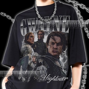 May include: A black short-sleeve t-shirt featuring a graphic print of characters in medieval armor with lightning effects. The text GWAYNE is printed in a metallic font at the top, and the word Hightower is printed in a script font at the bottom.