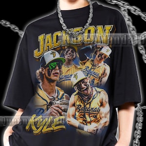 Peut inclure: Un t-shirt noir à manches courtes avec une impression graphique de joueurs de baseball en maillots jaunes, portant l'inscription "JACKSON" en haut et "KYLE" en bas. Les joueurs portent des casquettes avec des logos de banane.