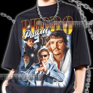 K&ouml;nnte beinhalten: Schwarzes T-Shirt mit einem Retro-Grafik von Pedro Pascal in verschiedenen Rollen, mit dem Namen "Pedro Pascal". Das Design enth&auml;lt Bilder des Schauspielers in verschiedenen Outfits. Eine silberne Kette wird getragen.
