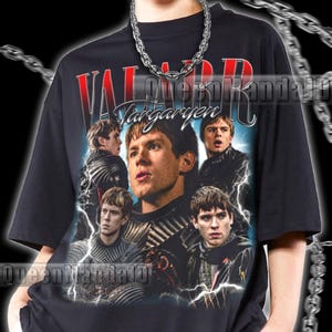 以下が含まれることがあります： 黒色のユニセックスTシャツ。男性のグラフィックと「VALAR Targaryen」の赤と白の文字が特徴です。デザインには、稲妻効果のある男性の複数の画像が含まれています。モデルは2XLシャツを着用しています。シャツはサイズ通りです。