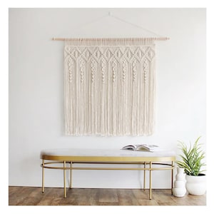 May include: A cream-colored macrame wall hanging with a geometric design is suspended from a wooden dowel. Below, a gold-framed bench with a marble top and a potted plant add to the room's decor. The bench is approximately 48 inches long.