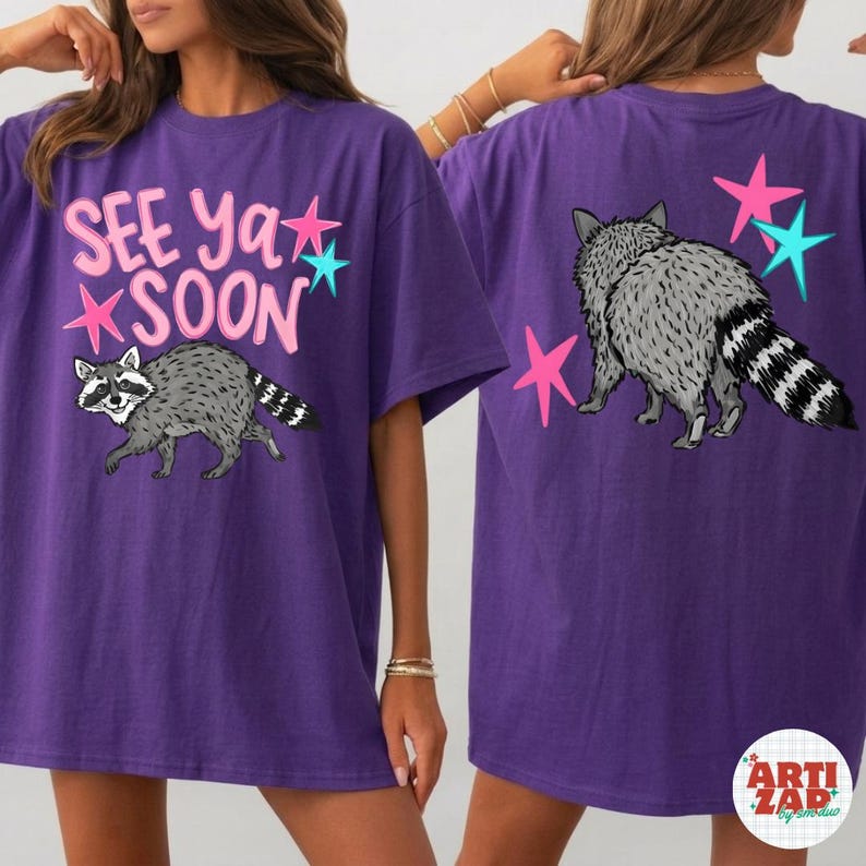 May include: Purple t-shirt with a raccoon graphic and the text "See Ya Soon". The design includes pink and teal stars. The back of the shirt features a raccoon and more stars.