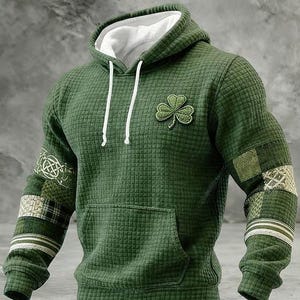 以下が含まれることがあります： 緑色のフード付きスウェットシャツ。テクスチャード加工のパターンと白い裏地が特徴です。胸にはクローバーのパッチ、袖には装飾パッチが付いています。フロントポケットと白いドローコードが含まれています。