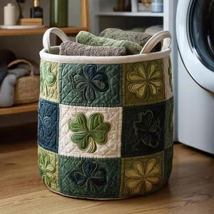 May include: A round, quilted laundry basket with a patchwork design featuring shamrock appliques in shades of green, blue, and cream. The basket has white handles and is filled with folded towels.