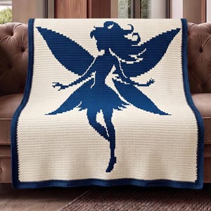 Könnte beinhalten: Eine cremefarbene Häkeldecke mit einem dunkelblauen Feen-Silhouette-Design. Die Decke hat einen dunkelblauen Rand und ist über einem braunen Sofa drapiert. Die Fee hat große Flügel und fließendes Haar.