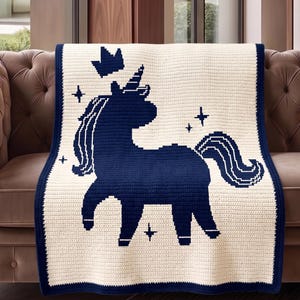 Pu&ograve; includere: Una coperta all'uncinetto color crema con un design a unicorno blu navy. La coperta presenta un bordo blu navy, una silhouette di unicorno, una corona e accenti di stelle. La coperta &egrave; drappeggiata su un divano marrone.