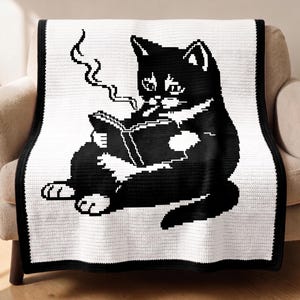 Può includere: Una coperta all'uncinetto in bianco e nero con un gatto che legge un libro e fuma. Il gatto è raffigurato in uno stile pixelato, con un cuore bianco sul petto. La coperta ha un bordo nero ed è drappeggiata su una poltrona beige.