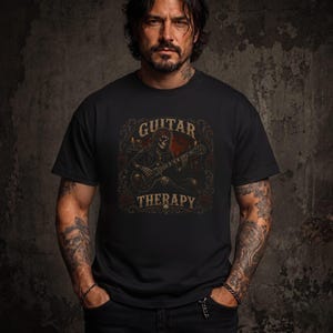 May include: A black short-sleeved t-shirt featuring a graphic print of a skeleton playing an electric guitar. The text "GUITAR THERAPY" is printed in a distressed font above and below the skeleton, surrounded by a decorative border of roses.