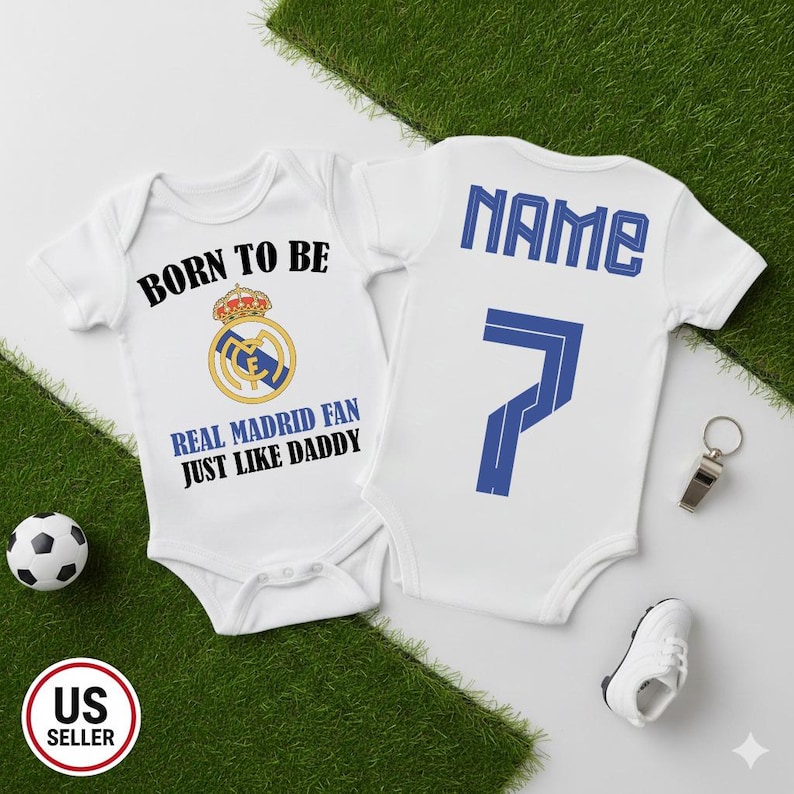 May include: Two white baby onesies with Real Madrid designs. One features the text "BORN TO BE REAL MADRID FAN JUST LIKE DADDY" and the team logo. The other has "NAME" and the number 7 in blue.