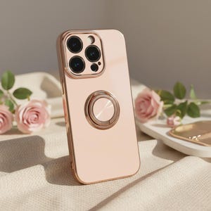 May include: A rose gold phone case with a ring holder. The case has a glossy finish and a metallic frame. The camera lenses are visible at the top. The ring holder is circular and metallic. The background includes pink roses and a white surface.