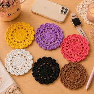 May include: A set of six round, crocheted coasters in yellow, purple, pink, white, black, and brown. Each coaster features a circular, intricate, openwork lace pattern with a scalloped edge, showcasing detailed yarn stitching and texture.