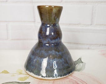 Pode incluir: Um vaso de cerâmica com base alargada e pescoço estreito, apresentando um esmalte brilhante que transita de um azul escuro profundo na base para um tom verde acastanhado no topo, com uma superfície lisa, reflexiva e abertura circular.