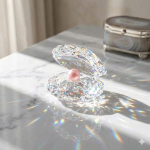 Pode incluir: Uma concha de cristal com uma p&eacute;rola rosa no interior. A concha est&aacute; aberta, revelando a p&eacute;rola. O cristal reflete a luz, criando um efeito arco-&iacute;ris. Uma pequena caixa decorativa est&aacute; ao fundo.