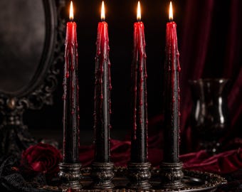 May include: Four tall taper candles with black bodies and red wax dripping from the top. Each candle is lit with a bright flame and stands in a dark, ornate, circular metal candle holder. The candles are arranged in a row on a dark tray.