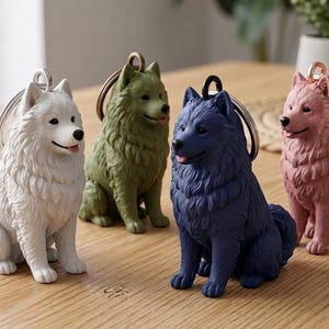 May include: Four dog-shaped keychains in white, green, navy blue, and pink. Each dog is sitting with a keyring attached to its head. The keychains are on a light brown wooden surface.