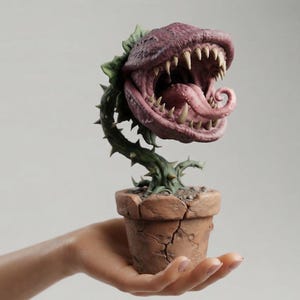 May include: A sculpted figurine of a carnivorous plant with a wide, open mouth featuring sharp, pointed teeth and a long, curled tongue. The plant has a green, thorny stem and is potted in a textured, cracked, light brown clay-like container.