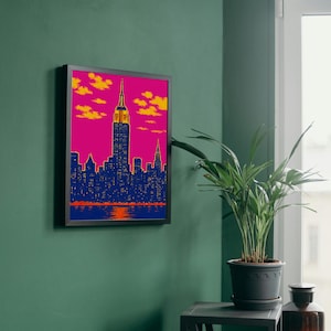 以下が含まれることがあります： 夕焼け時のニューヨークのスカイラインを描いた額入りアートプリント。エンパイアステートビルや他の高層ビルがピクセル化されたスタイルで描かれ、鮮やかなピンク色の空とオレンジ色の雲が特徴です。フレームは黒色です。