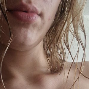 Può includere: Primo piano del viso e della spalla di una persona, con capelli bagnati e castano chiaro. Le labbra della persona sono leggermente socchiuse. L'incarnato è chiaro. Lo sfondo è di colore chiaro.