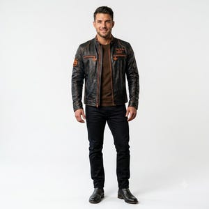 Könnte beinhalten: Eine schwarze Lederjacke mit orangefarbenen Nähten, Stehkragen und Frontreißverschluss. Auf der Brust befindet sich der orangefarbene Schriftzug "TREX OR TREAT" und auf dem rechten Ärmel ein kleiner orangefarbener Kürbisaufnäher über einem braunen Shirt.
