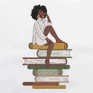 May include: An embroidery design featuring a person with dark skin and a large afro hairstyle, wearing a white collared shirt and gold hoop earrings, sitting atop a vertical stack of six books in various colors including yellow, green, and brown.