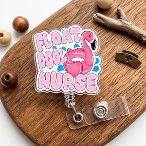 May include: A pink and white badge reel with the words "FLOAT POOL NURSE" and a flamingo in a pool float. The badge reel has a clear plastic strap and a metal clip for attaching to clothing.