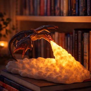 May include: A dragon-shaped lamp with a fiery breath effect. The dragon is dark brown with red accents, perched above a cloud-like base. The lamp emits a warm, orange glow, resting on a stack of books. The text "BooksKingdom" is visible.