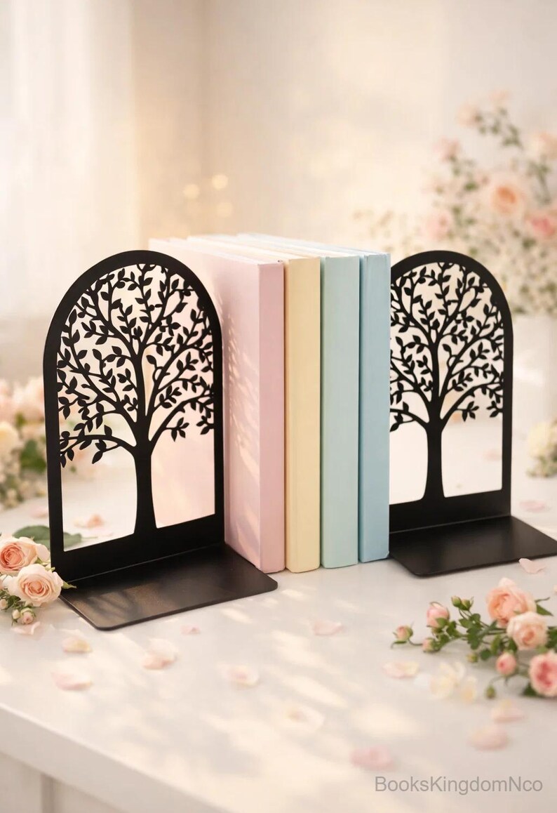 May include: Black metal tree design bookends holding pastel-colored books. The bookends have a cutout tree design and a rectangular base. The books are in shades of pink, yellow, and blue. The scene is decorated with flowers and petals.