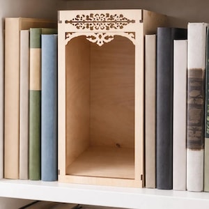 Könnte beinhalten: Ein helles Holzregalelement mit gewölbtem Oberteil und dekorativen Ausschnitten. Das Regal ist von Büchern in verschiedenen Farben und Größen umgeben, was eine ansprechende Darstellung ergibt. Das Regal ist leer.