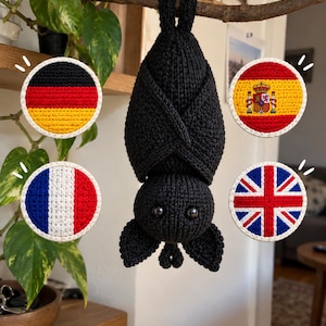 Peut inclure: Une chauve-souris noire crochetée suspendue la tête en bas, entourée de quatre écussons circulaires crochetés représentant les drapeaux nationaux de l'Allemagne, de l'Espagne, de la France et du Royaume-Uni, avec une bordure blanche.