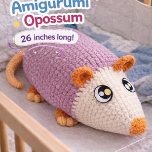 Puede incluir: Un peluche de zarigüeya amigurumi hecho a mano, de unos 66 cm de largo. El peluche presenta un cuerpo lavanda, una cara color crema y orejas y pies naranjas. El texto "Plump Amigurumi Opossum" se muestra encima del juguete.