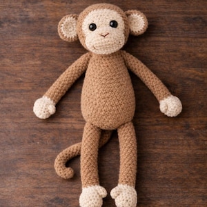 May include: A crocheted monkey toy featuring a light brown body, a cream-coloured face, ears, hands, and feet. The stuffed animal has black plastic eyes, a stitched nose and mouth, and a long, curved tail. The texture is consistent throughout.