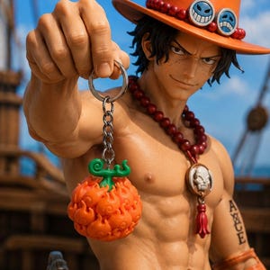 Könnte beinhalten: Detaillierte Figur eines Charakters aus der Anime-Serie One Piece. Die Figur trägt einen orangefarbenen Hut mit lächelnden Gesichts-Emblemen und eine rote Perlenkette. Er hält einen Schlüsselanhänger mit einer orangefarbenen, flammenartigen Frucht.