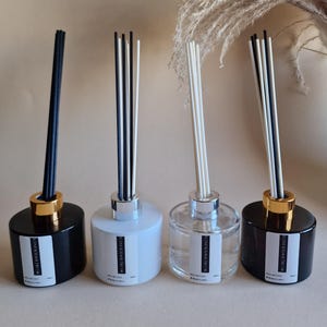 Pode incluir: Quatro difusores de varetas com frascos de vidro preto, branco e transparente. Os frascos pretos têm detalhes dourados, enquanto os brancos e transparentes têm detalhes prateados. Cada difusor tem um rótulo com "SCENT & SENSE DECOR".