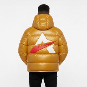 May include: Mustard-colored puffer jacket with a hood. The back of the jacket features a white and red logo. The jacket is worn over black pants. The jacket is a shiny material.