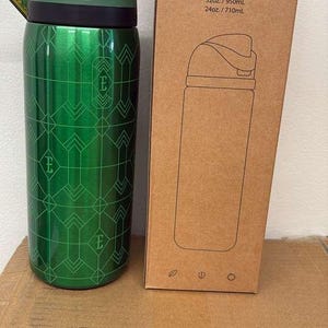 May include: A green Owala Free Sip water bottle with a geometric pattern and a black and green lid. The bottle is 32oz / 950mL. The box next to it has the words "Free Sip" and a drawing of the bottle.